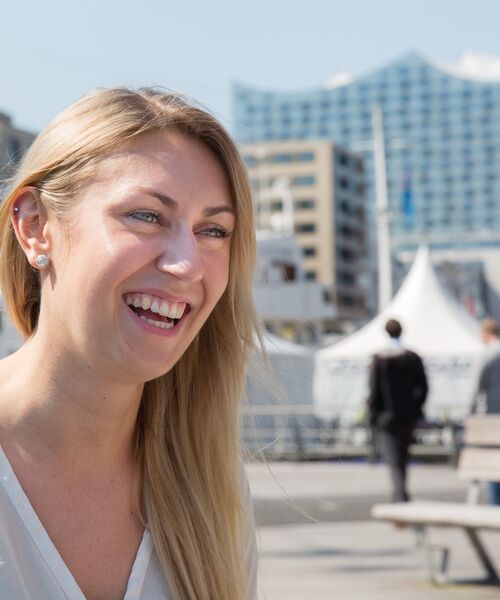 Junge Frau lacht im Freien, im Hintergrund moderne Architektur und die Elbphilharmonie.