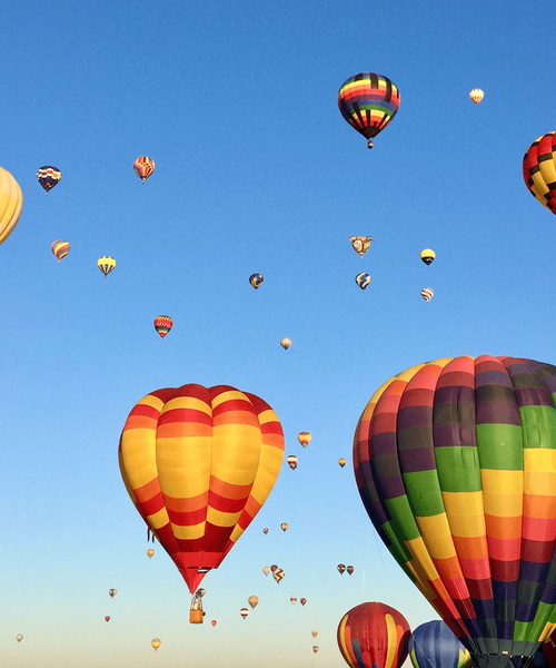 Mehrere bunte Heißluftballons steigen bei klarem Himmel in die Luft.