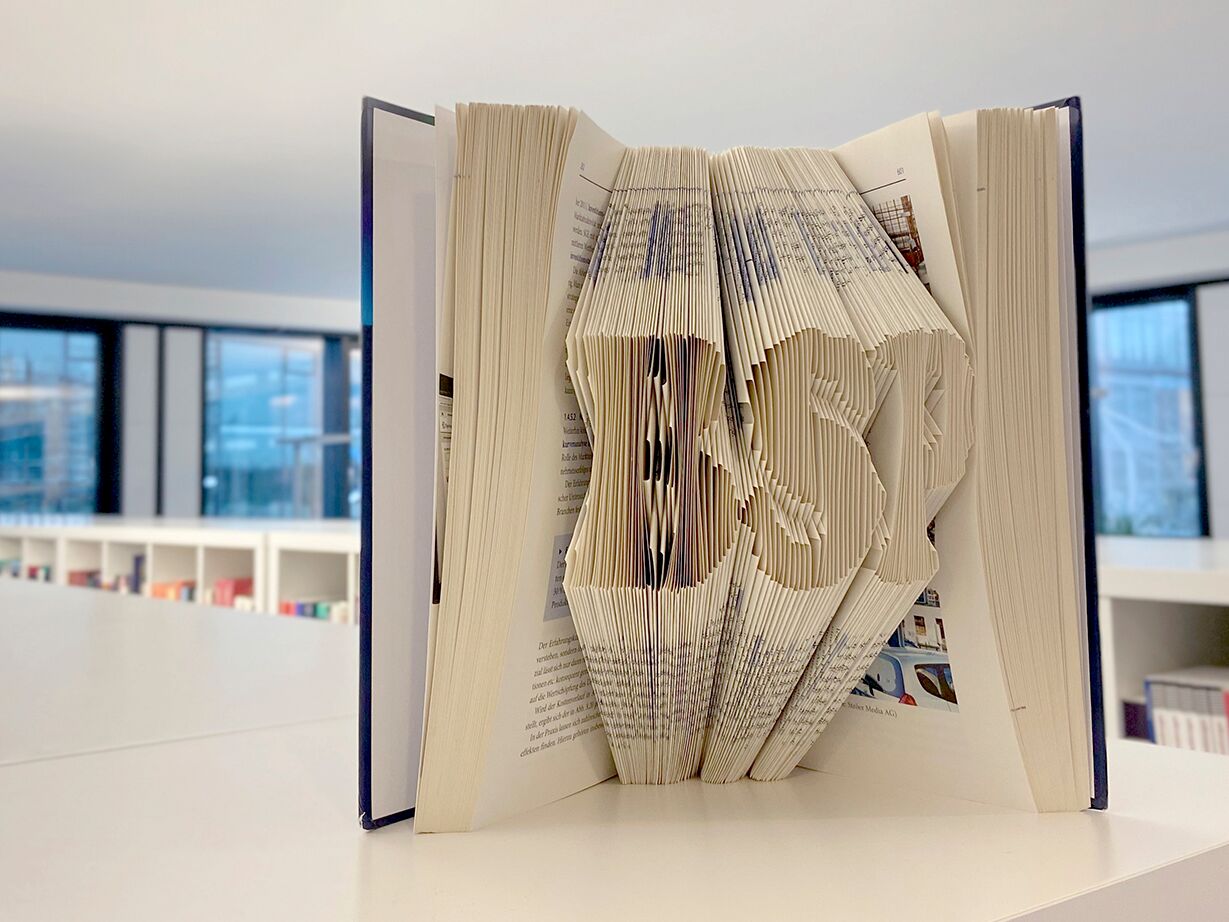 Aufgeschlagenes Buch mit kunstvoll gefalteten Seiten, die die Buchstaben „BSP“ formen.