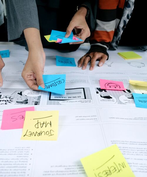 Personen ordnen bunte Haftnotizen auf einem Arbeitspapier für ein Workshop-Konzept.