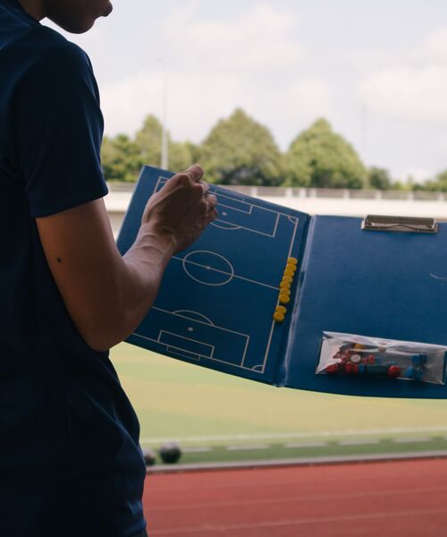 Trainer hält eine Taktiktafel mit Spielfeldskizze am Spielfeldrand.