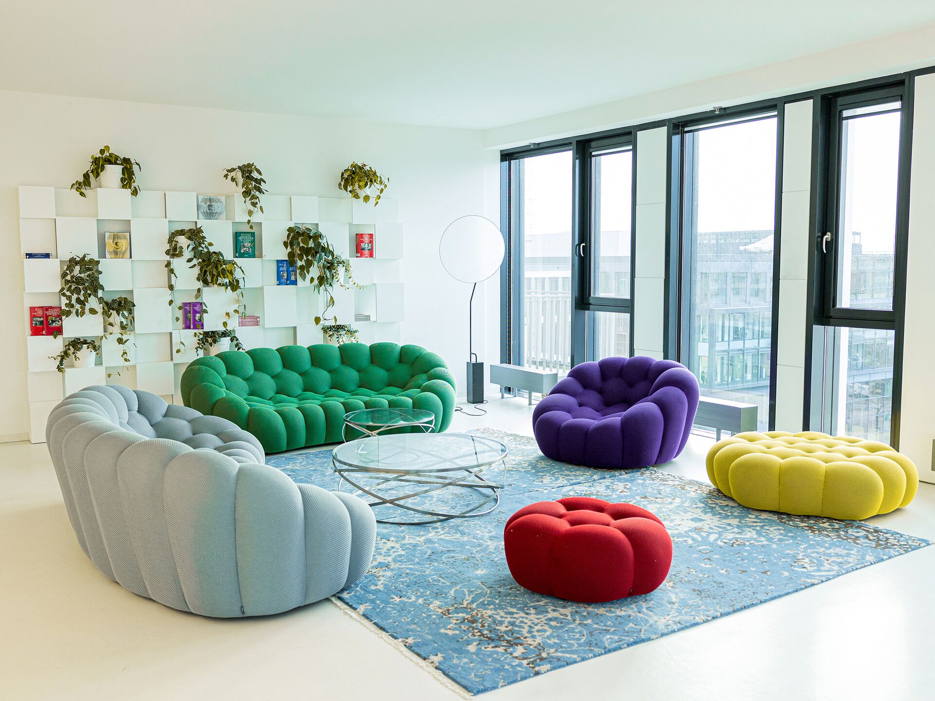 Heller Lounge-Bereich mit bunten Polstermöbeln, Glas-Couchtisch und großen Fenstern.
