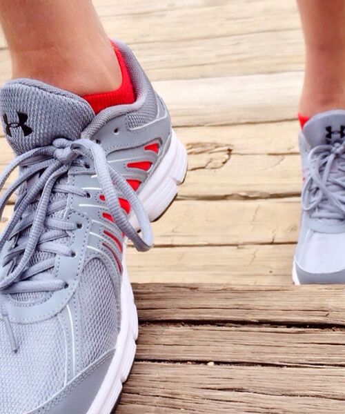 Graue Laufschuhe mit roten Akzenten auf einem hölzernen Steg.