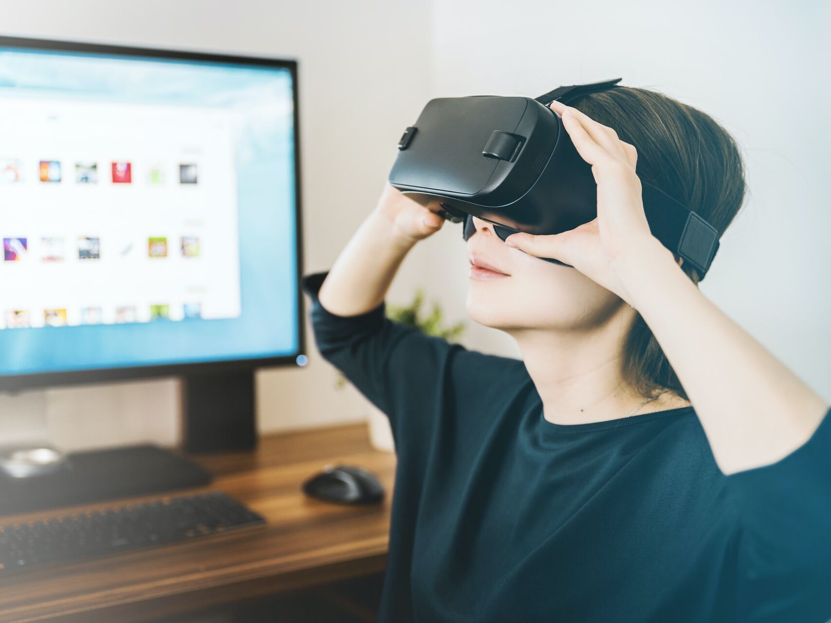 Person mit Virtual-Reality-Brille vor einem Computerbildschirm.