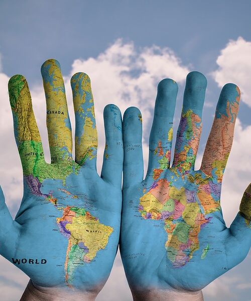 Zwei Hände mit aufgemalter Weltkarte vor blauem Himmel.
