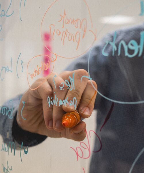 Person schreibt mit einem Marker Notizen und Diagramme auf eine Glaswand.