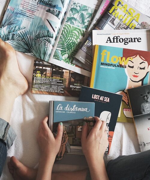 Person liest ein Magazin, umgeben von weiteren bunt gestalteten Zeitschriften.