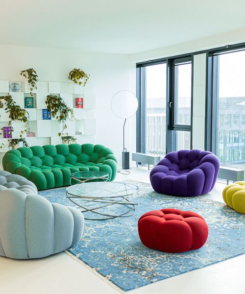 Heller Lounge-Bereich mit bunten Polstermöbeln, Glas-Couchtisch und großen Fenstern.