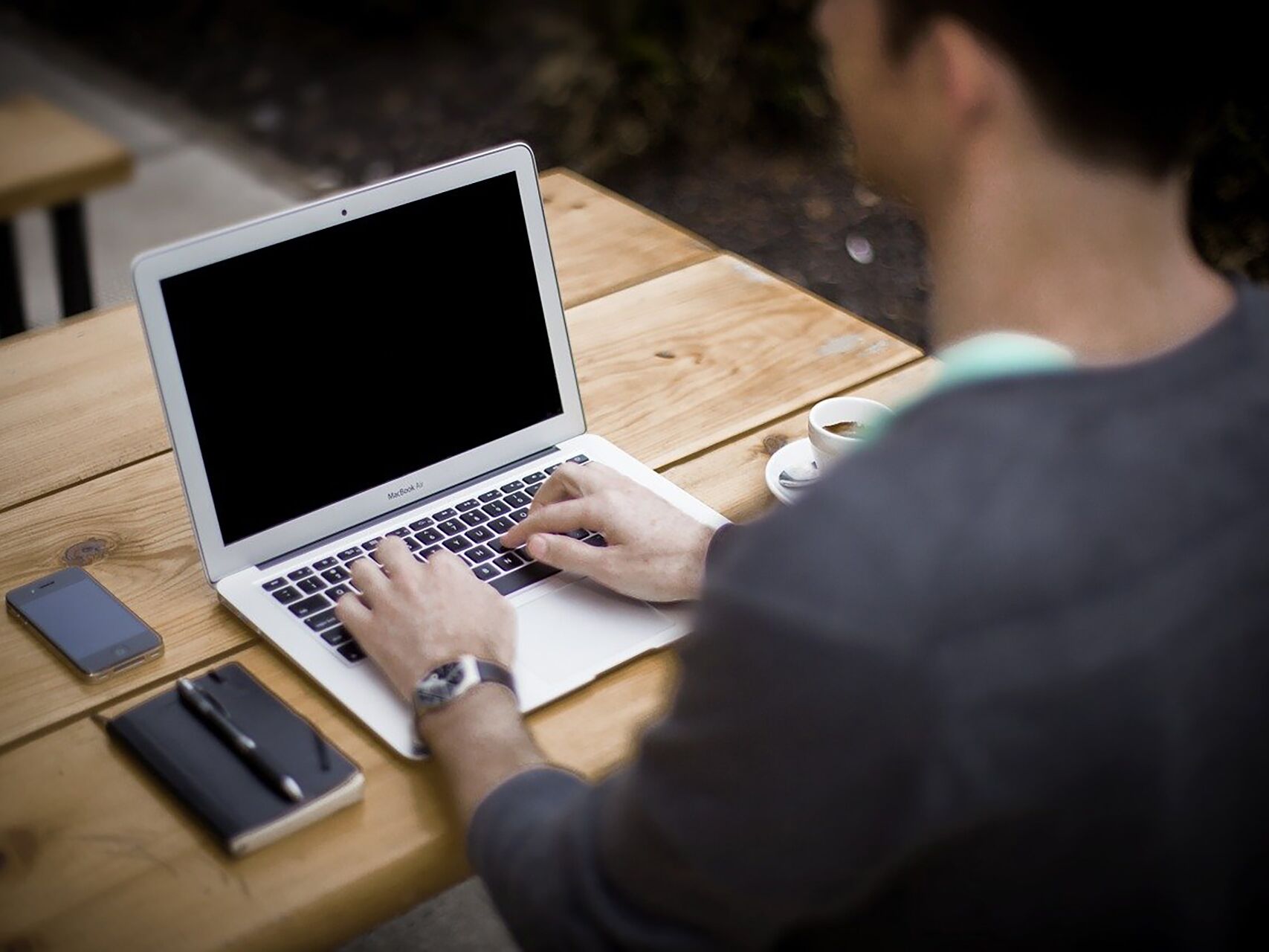 Person arbeitet im Freien an einem Laptop mit einer Tasse Kaffee daneben.