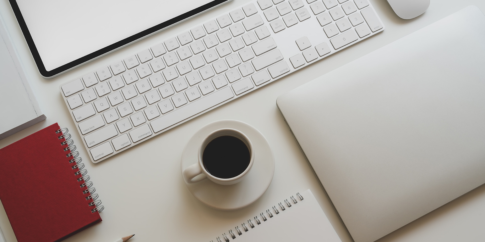 Schreibtisch mit Laptop, Tastatur, Notizbüchern und einer Tasse Kaffee in minimalistischer Anordnung.