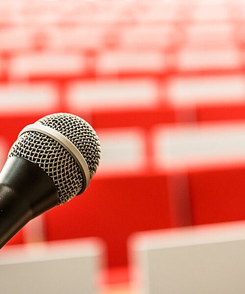 Nahaufnahme eines Mikrofons mit unscharfen roten Sitzreihen im Hintergrund.
