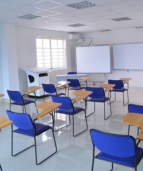 Moderner Klassenraum mit blauen Stühlen, Pult und Whiteboards.