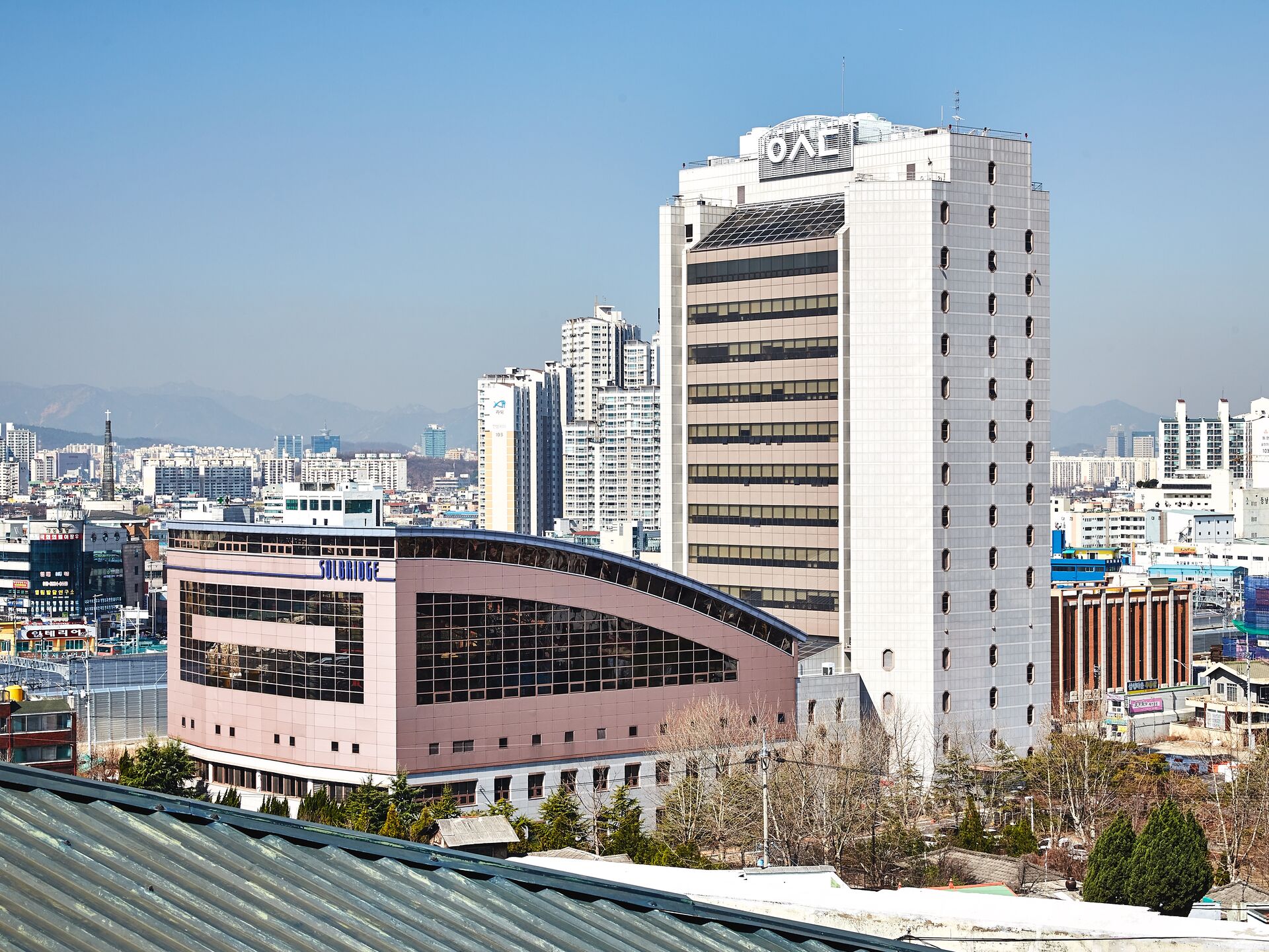 Großer Universitätscampus mit modernem Hochhaus und angrenzendem Gebäude inmitten einer Stadt.