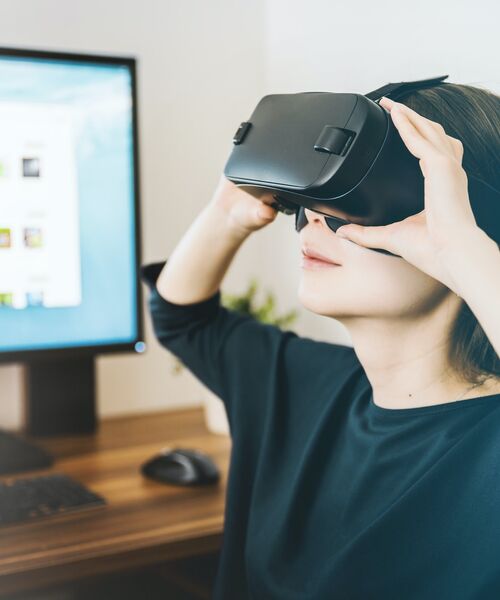 Person mit Virtual-Reality-Brille vor einem Computerbildschirm.