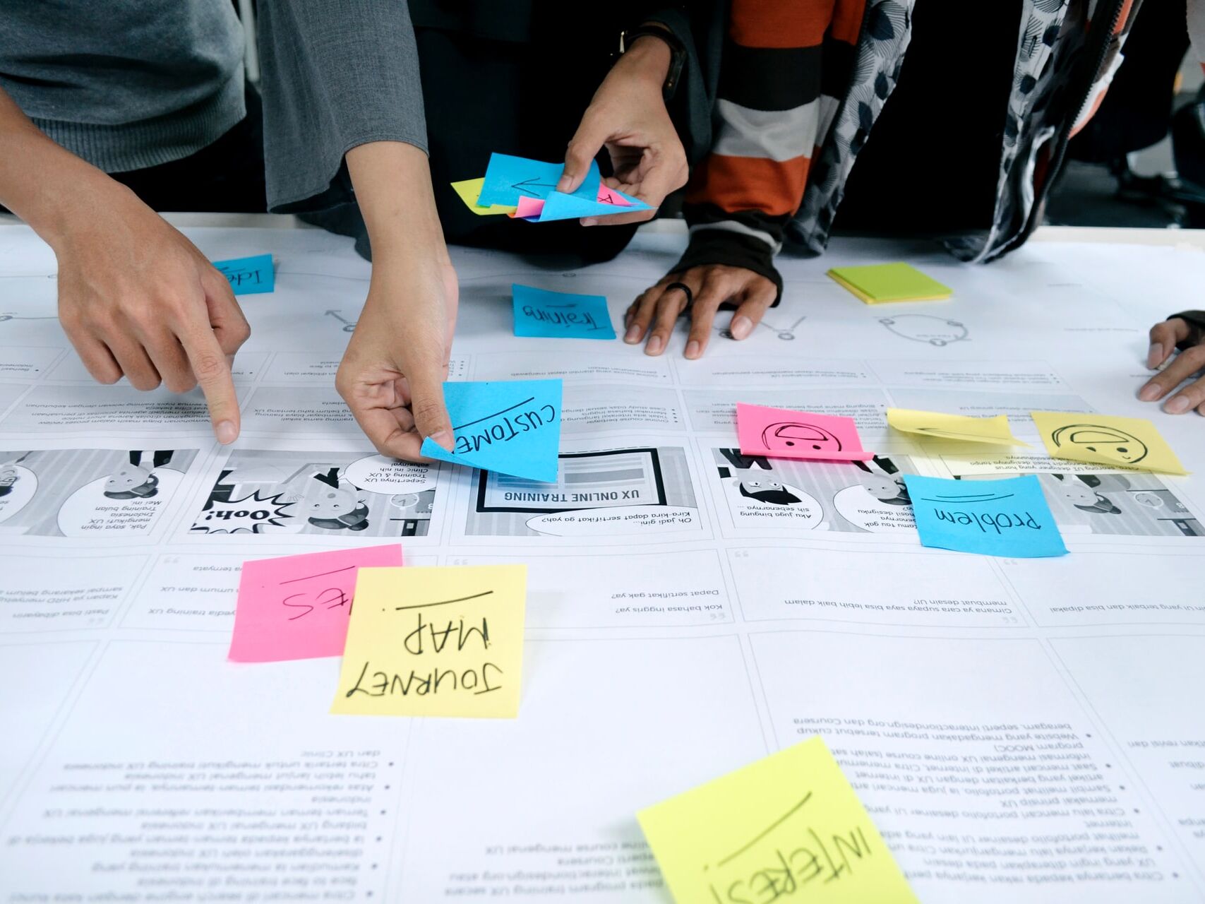Personen ordnen bunte Haftnotizen auf einem Arbeitspapier für ein Workshop-Konzept.
