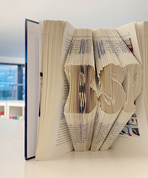 Aufgeschlagenes Buch mit kunstvoll gefalteten Seiten, die die Buchstaben „BSP“ formen.