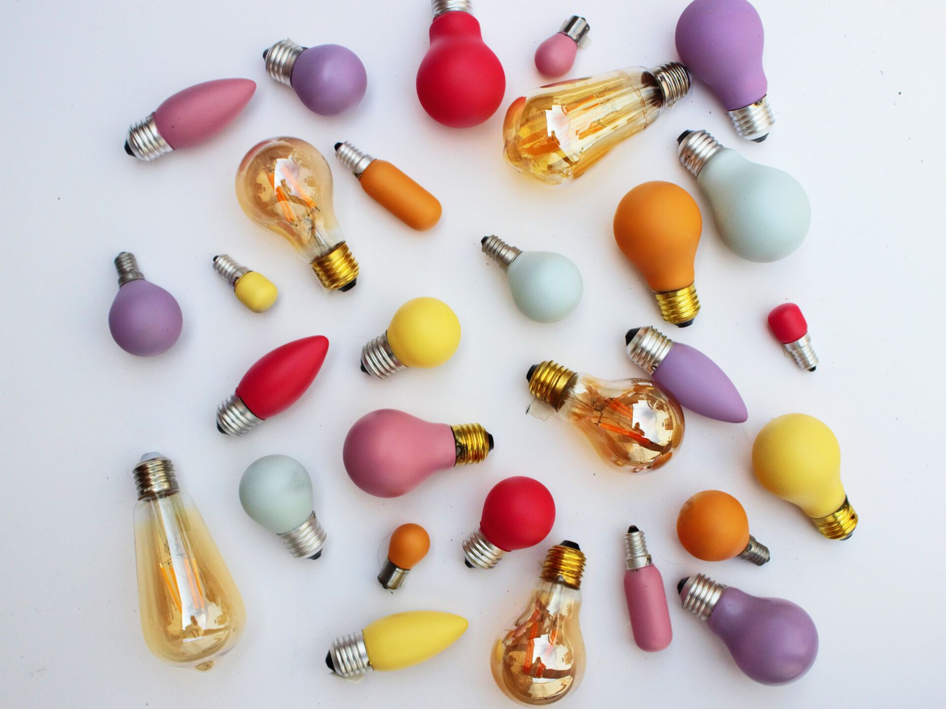 Bunte Glühbirnen in verschiedenen Formen und Farben auf weißem Hintergrund.