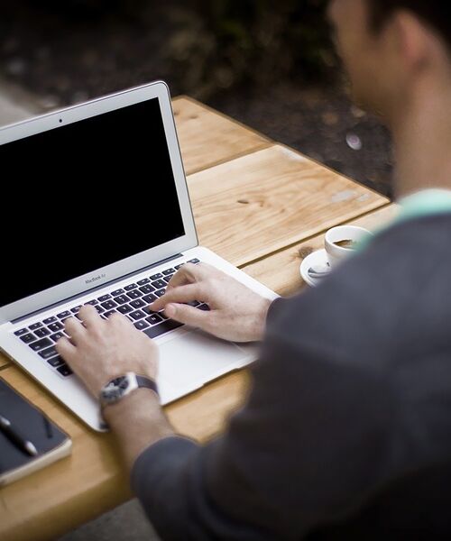 Person arbeitet im Freien an einem Laptop mit einer Tasse Kaffee daneben.