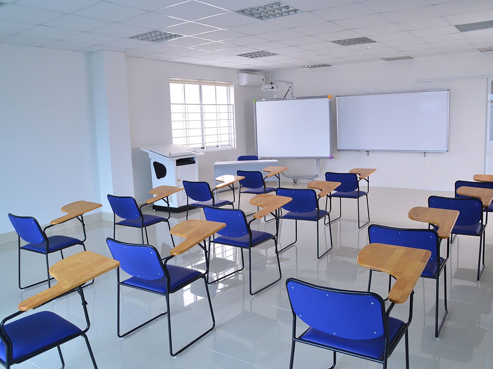 Moderner Klassenraum mit blauen Stühlen, Pult und Whiteboards.