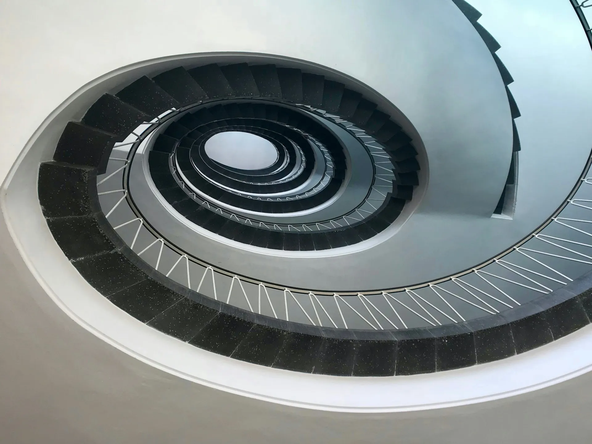 Blick nach oben in ein spiralförmiges Treppenhaus mit schwarzen Stufen und weißen Geländern.