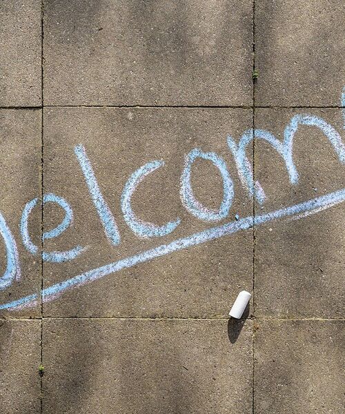 Mit Kreide auf den Boden geschriebenes „Welcome“ als Willkommensgruß.