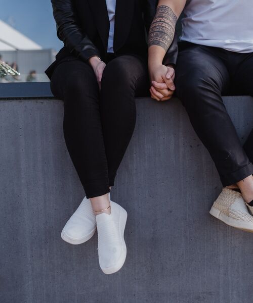 Zwei Personen sitzen nebeneinander auf einer Mauer und halten sich an den Händen.