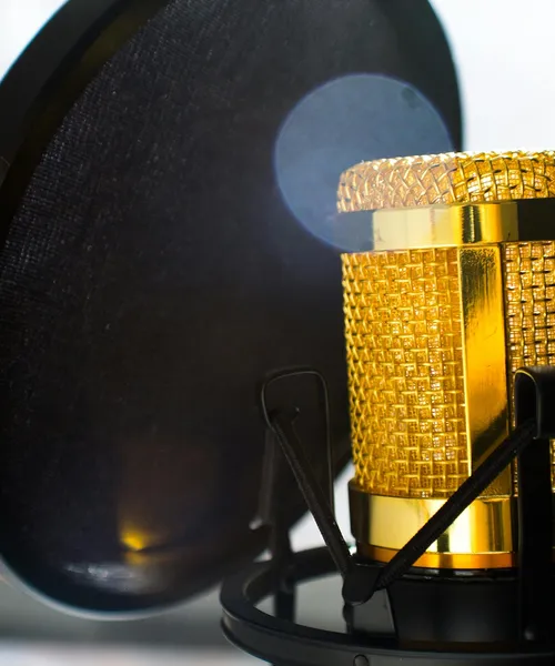 Nahaufnahme eines goldfarbenen Mikrofons mit Popschutz im Aufnahmestudio.